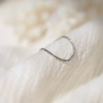 Delicate platinum chain link ring with small glints of light reflecting off the surface on a soft beige fabric background