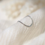 Delicate platinum chain link ring with small glints of light reflecting off the surface on a soft beige fabric background