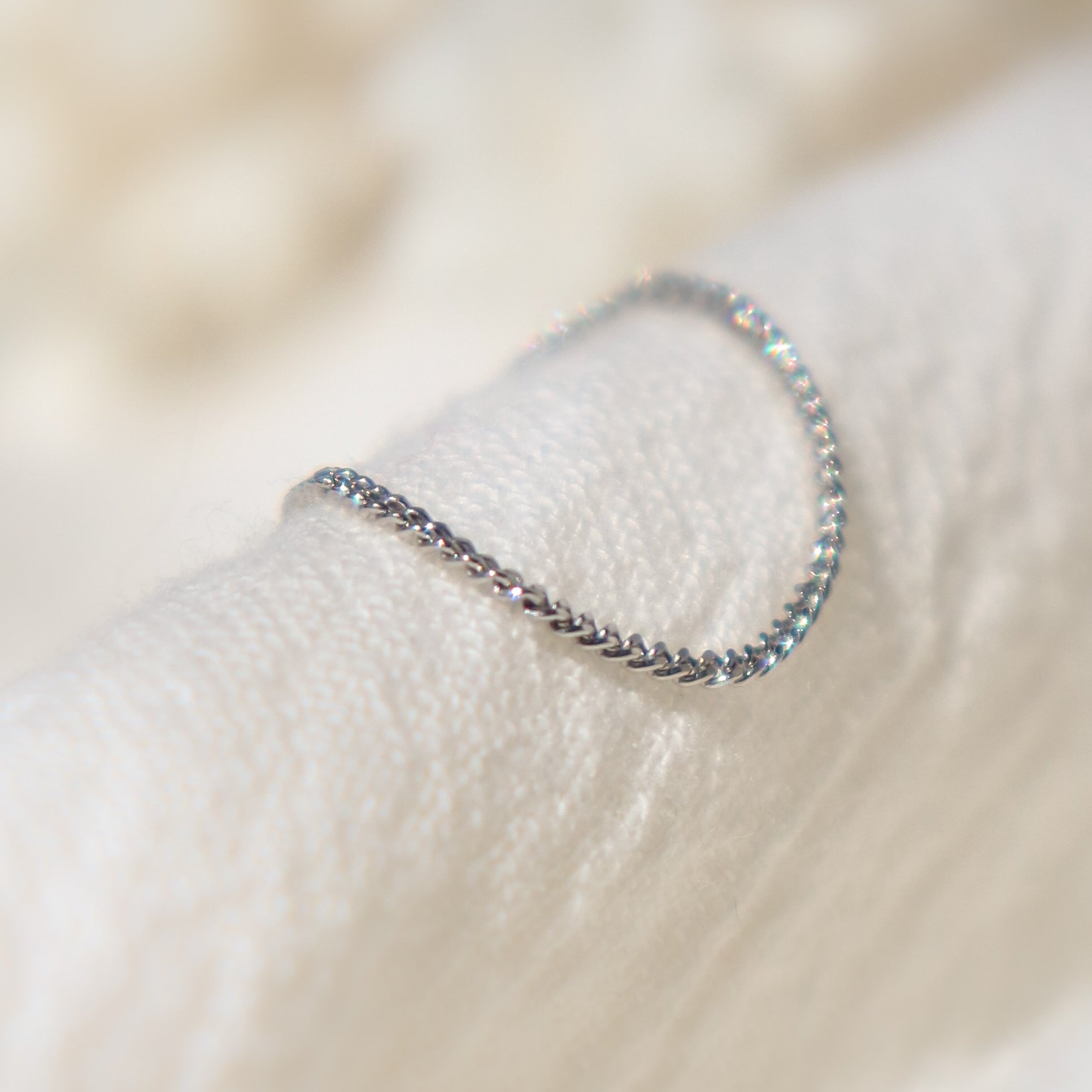 Delicate solid platinum chain ring for women on a textured beige surface