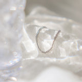Platinum chain link finger ring for women on a textured white surface with water like shadows reflecting off the background and a crystal glass blurred out off to the side.