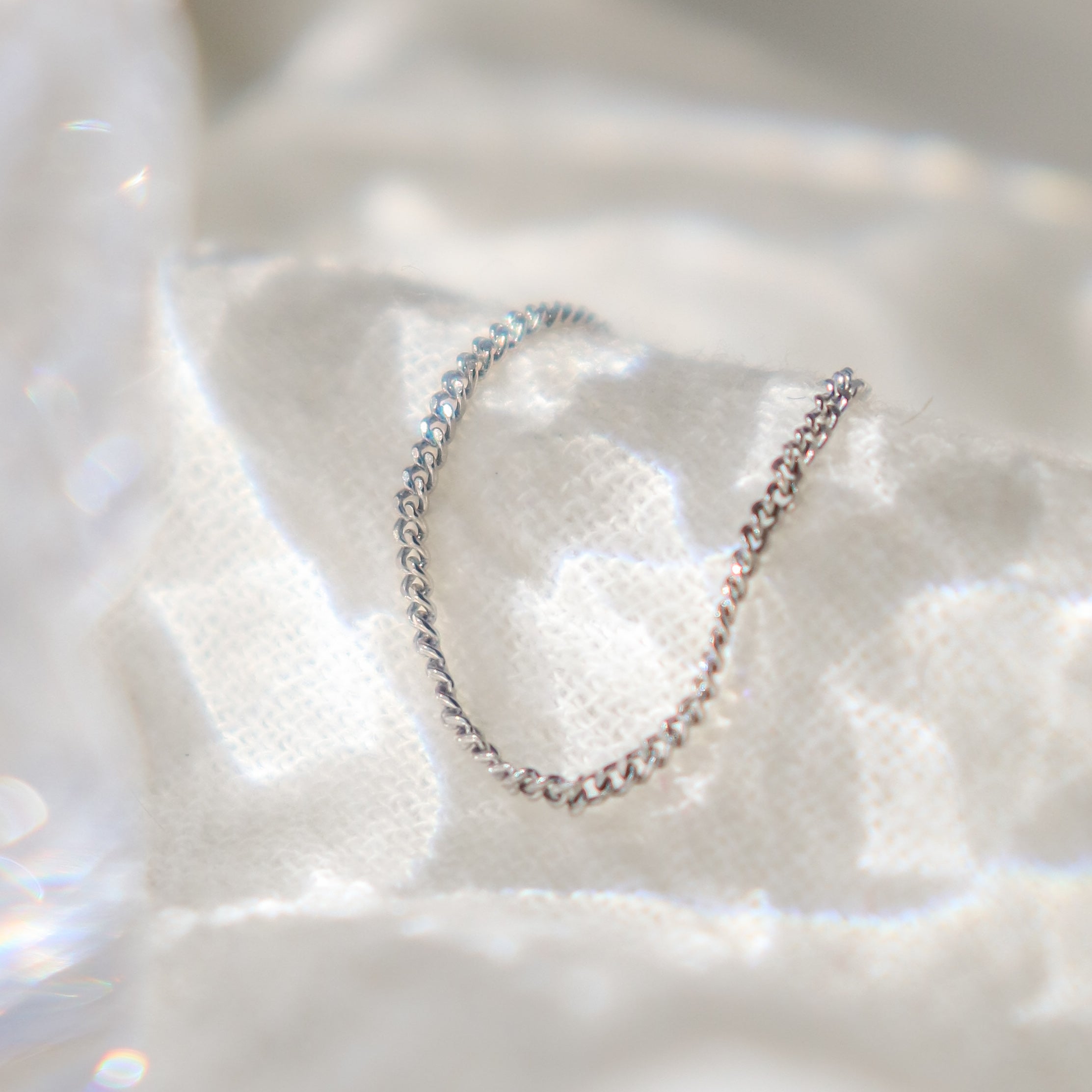 Platinum chain link finger ring for women on a textured white surface with water like shadows reflecting off the background.