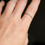 Woman's hand wearing a petite, thin platinum chain ring on a dark background