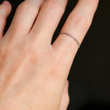 Woman's hand wearing a petite, thin platinum chain ring on a dark background