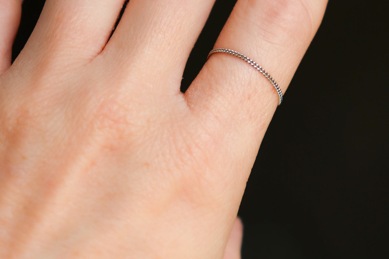 Woman's hand wearing a petite, thin platinum chain ring on a dark background