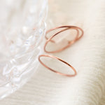 A close-up of three smooth, rounded band solid 14k rose gold stacking rings on a textured white surface.