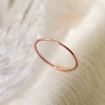 One smooth, round women's finger ring in rose gold is positioned upright on a light fabric and blurred crystal background.