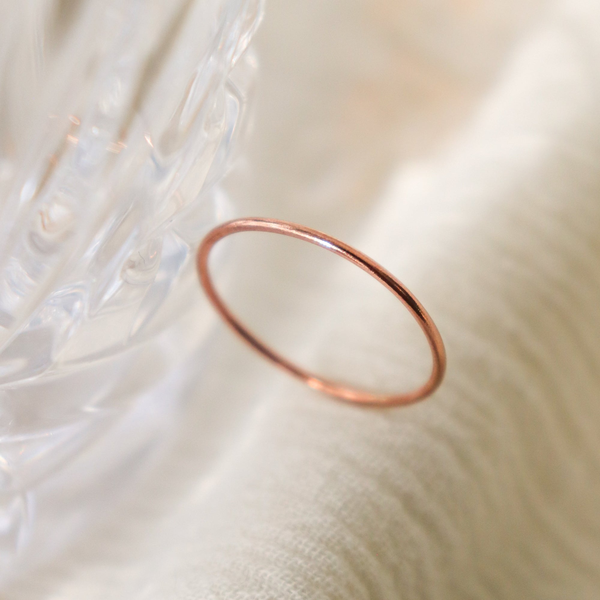 One smooth, round women's finger ring in rose gold is positioned upright on a light fabric and blurred crystal background.