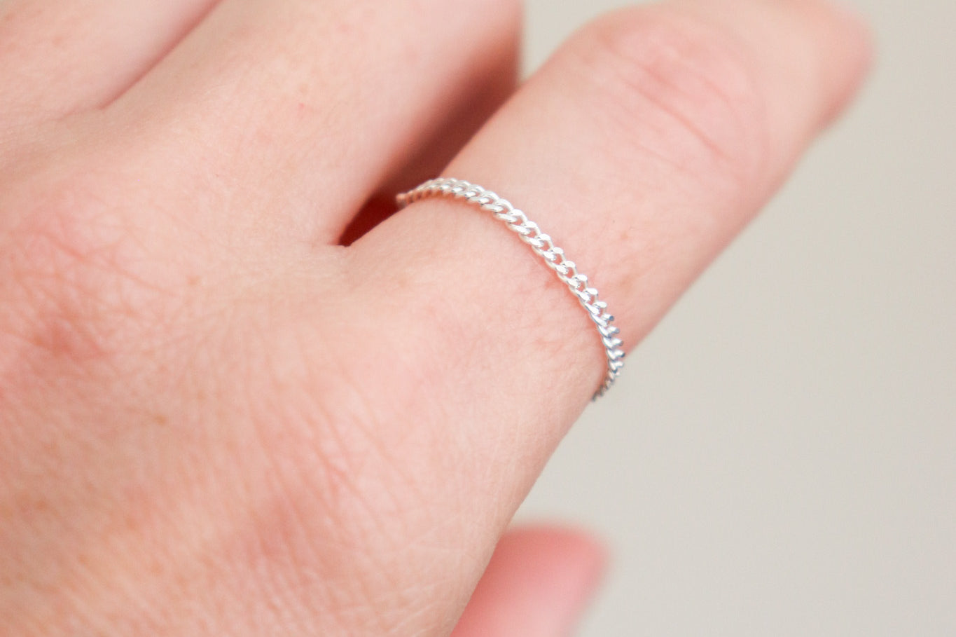 Silver ring on a woman's finger against a neutral background