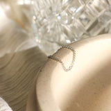 Silver chain link ring on a light beige ceramic dish in dramatic golden hour lighting with blurred crystal background.