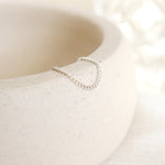 Women's dainty silver chain link ring draped over the side of a pottery dish with a soft beige background