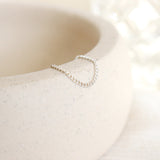 Women's dainty silver chain link ring draped over the side of a pottery dish with a soft beige background
