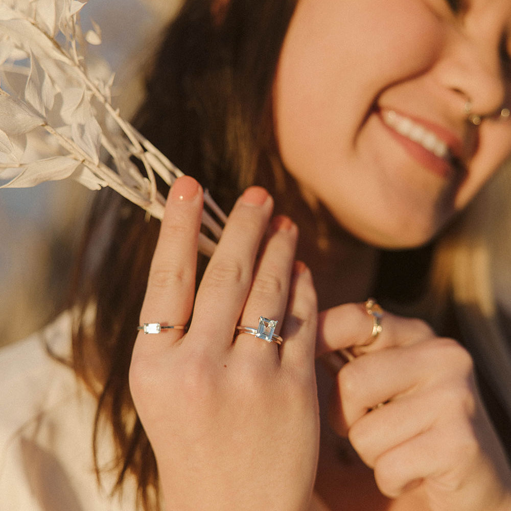 A smiling woman holding a dried floral element close to hear face is wearing luxury gemstone jewelry