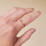 Hand wearing a gold beaded ring and a gold chain ring on a beige background