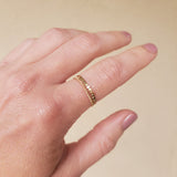 Hand wearing a gold beaded ring and a gold chain ring on a beige background