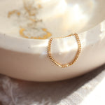 Women's modern, minimalist 14k gold chain ring on a light beige ceramic dish with a blurred background.