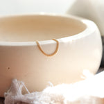 Gold minimalist chain ring on a white ceramic bowl with a soft focus background