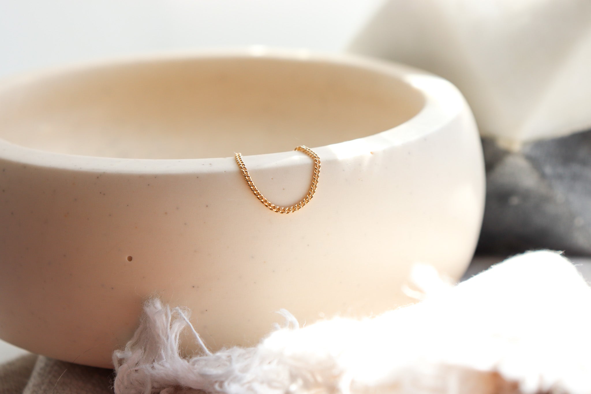 Gold minimalist chain ring on a white ceramic bowl with a soft focus background