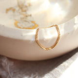 Gold chain ring on a white ceramic dish with a blurred background that has some glints of gold.