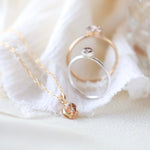 Gold memorial necklace and two memorial rings in silver and gold balanced upright on a light creamy and white fabric background.