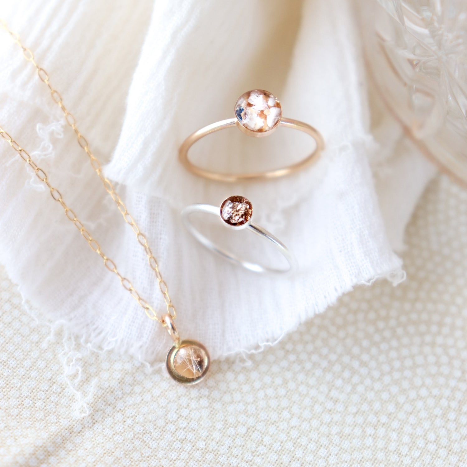 Round gold memorial pendant on a necklace necklace and two memorial rings with  on a white fabric background flat lay.