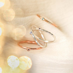Four minimalist personalized initial and symbol rings hand stamped on a tiny droplet soldered to each ring. The rings are balanced on a light, blurred background. The rings are mixed metals and textures - smooth and pebble hammered - in yellow gold fill, rose gold fill and solid sterling silver. The letters are M & and the symbols are a tiny heart and a tiny paw print.
