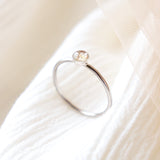 Platinum memorial ring with light colored ashes in a 4 mm clear resin setting. Featured sitting upright to see the size of the bezel setting on a soft beige fabric background.