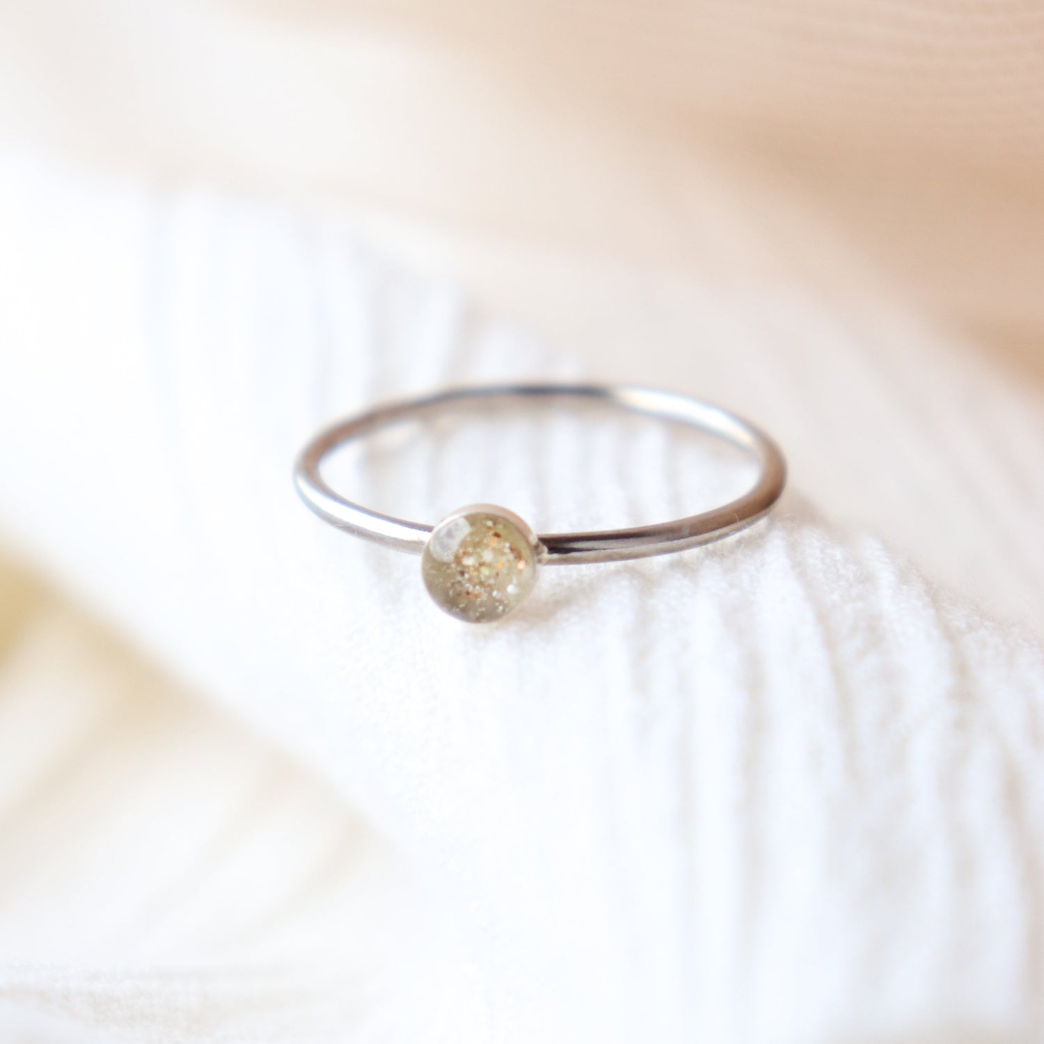 Platinum memorial ring with light colored ashes in a 4 mm clear resin setting. Featured on a light fabric background.