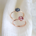 Yellow gold and 14k rose gold ashes rings on a light background. The rose ring features pink coloring and the yellow gold ring has dark sapphire coloring.