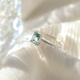 Rectangle shaped natural moss agate gemstone ring in a solid sterling silver setting with a smooth, round band. The ring is poised on a soft fabric background with moody lighting.
