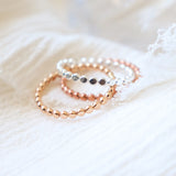 Set of three beaded womens finger rings in yellow gold, rose gold and sterling silver on a soft fabric background.