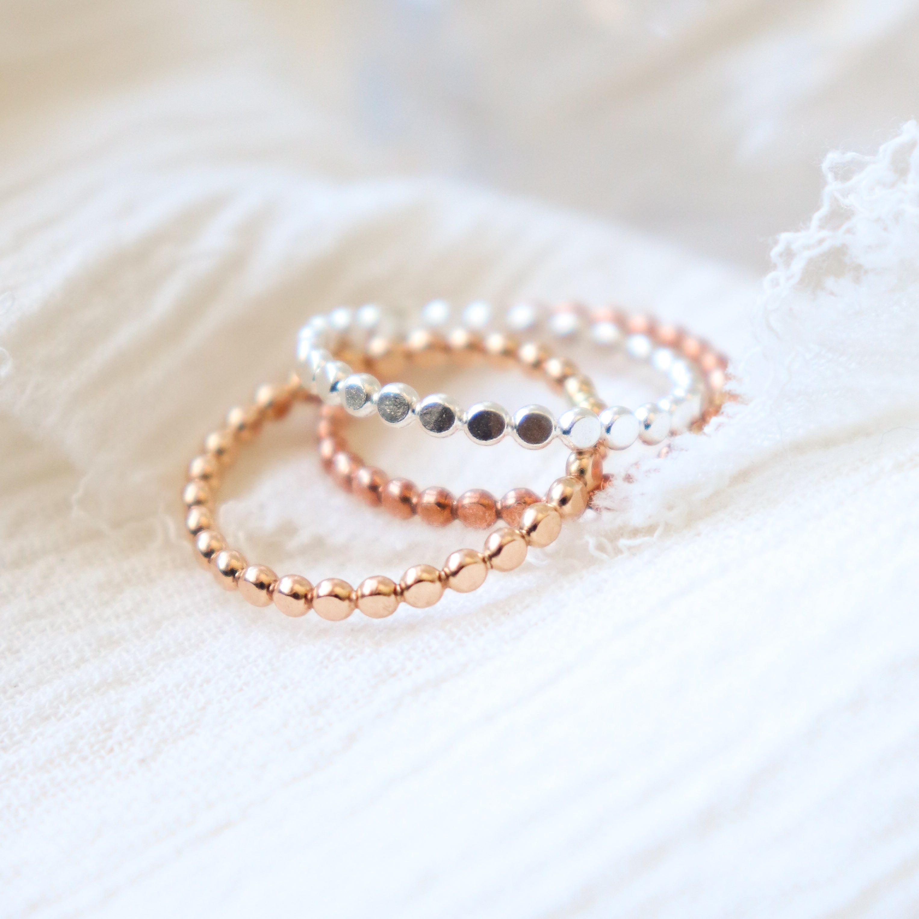 Set of three beaded womens finger rings in yellow gold, rose gold and sterling silver on a soft fabric background.