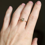 Solid gold moss agate ring on a woman's hand shown close up. The moss agate is a soft, ethereal, mossy fern green color with muted light filtering through the 4x6 mm emerald cut rectangle gemstone.