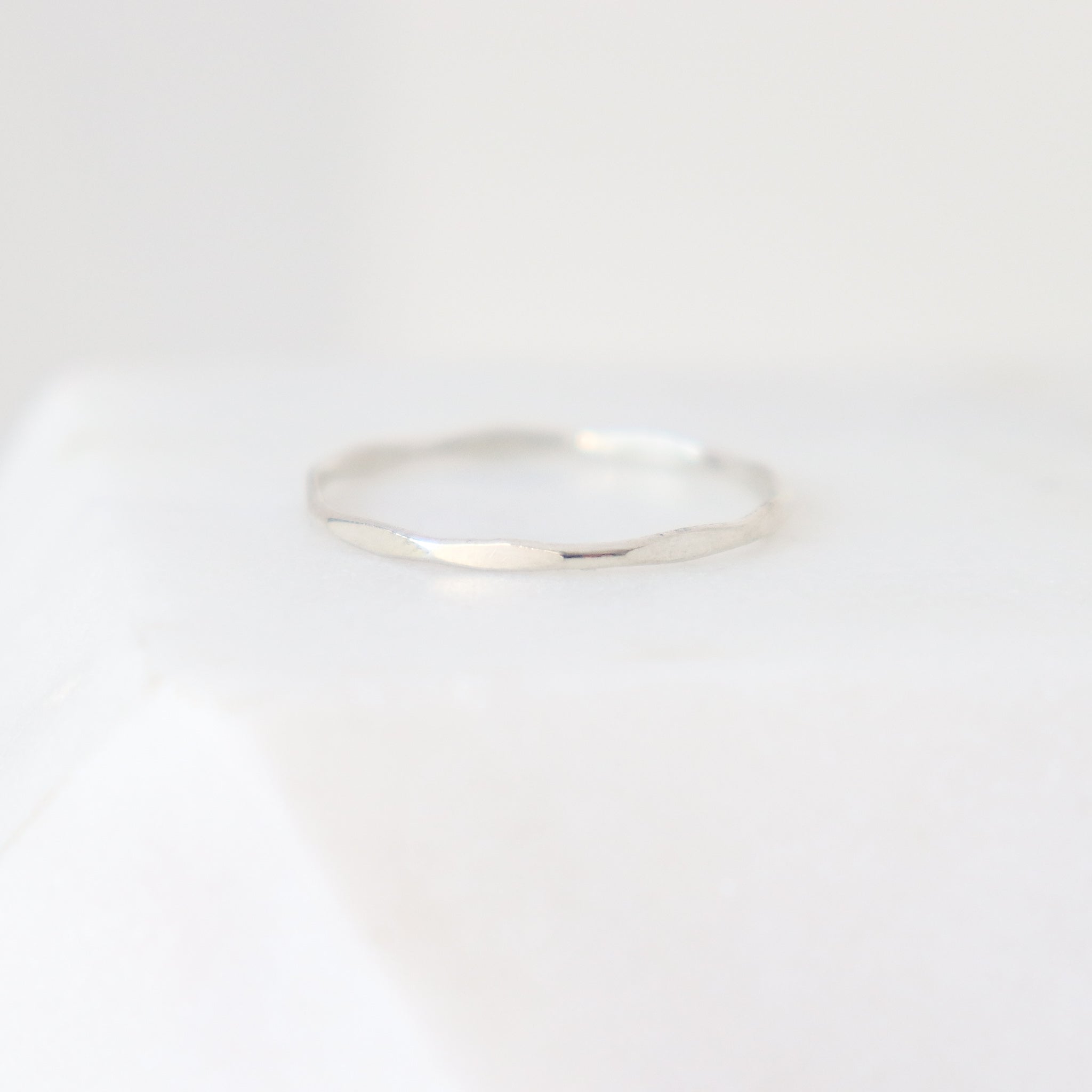 Slim sterling silver women's finger ring on a light gray background. The ring has a uniformly hammered or scalloped finish.