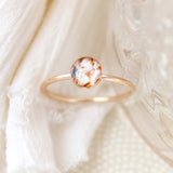 Close up detail of a solid 14k yellow gold cremation memorial ring with light colored ashes included in the resin setting on a light fabric and glass background that's softly blurred.