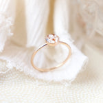 Close up detail of a solid 14k yellow gold cremation memorial ring with light colored ashes included in the resin setting on a light fabric background that's softly blurred. The ring is balanced upright to see the side profile.